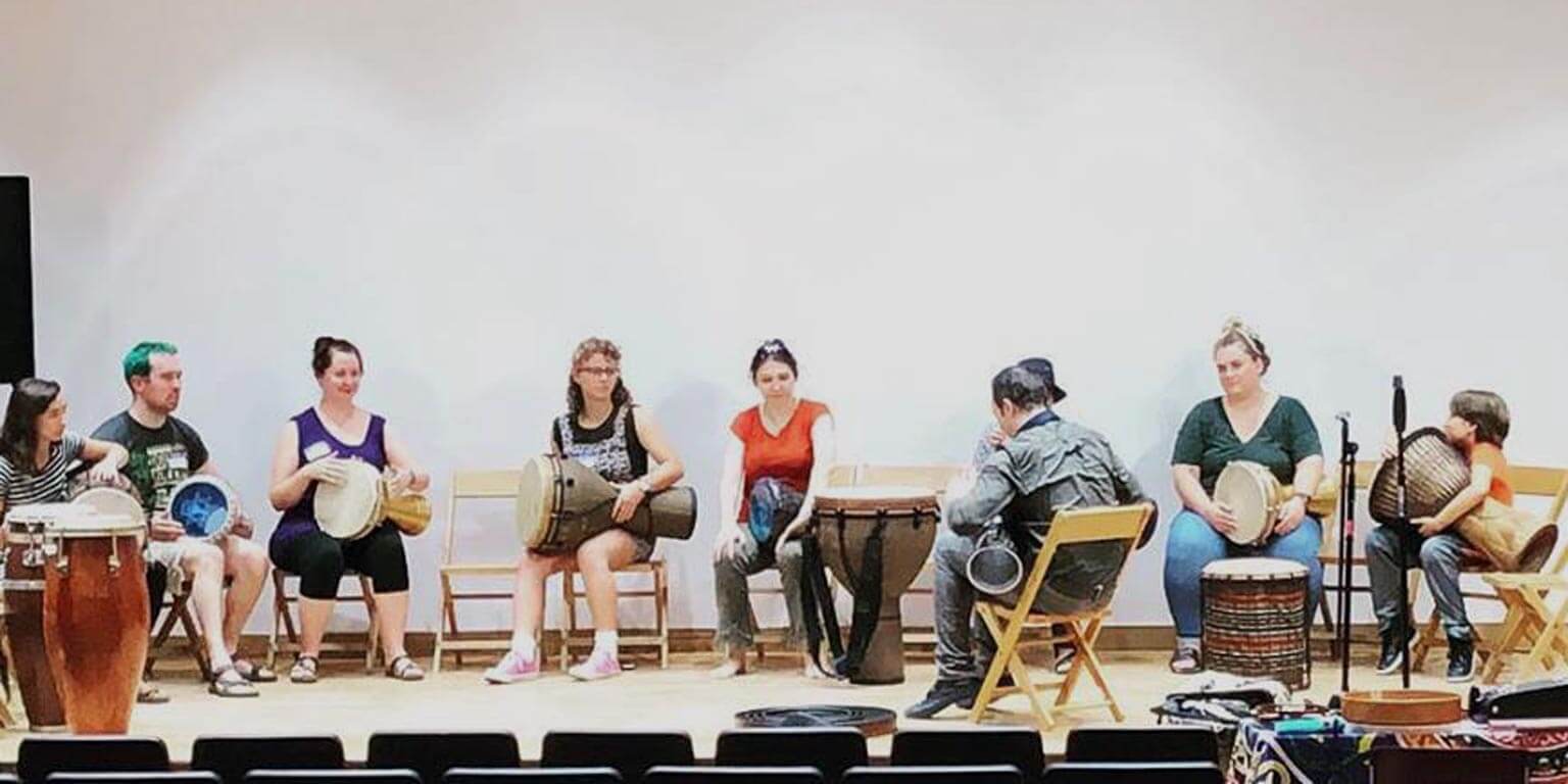 students sit around a circle and play drums